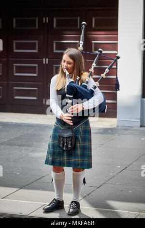 Young girl bagpiper playing bagpipes on street outside in city Glasgow, Scotland iconic Scottish sight piper sounds in kilt Stock Photo
