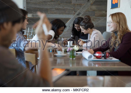 Young women friends drinking coffee, using smart phone in cafe