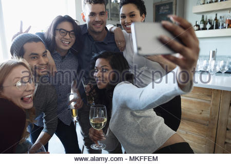 Playful young friends with camera phone taking selfie, enjoying happy hour, drinking wine