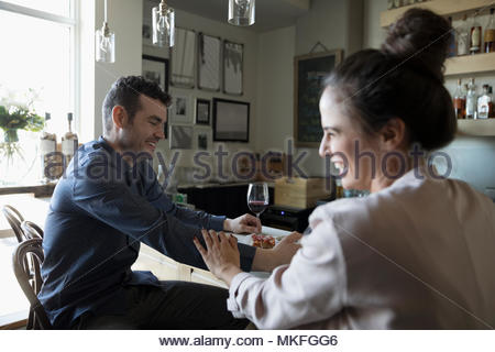 Young couple on date, laughing and drinking red wine in bar