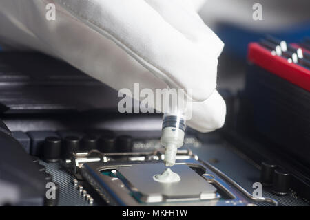 Hand wearing White Gloves with syringe applying thermal paste on the CPU processor on motherboard Close up Stock Photo