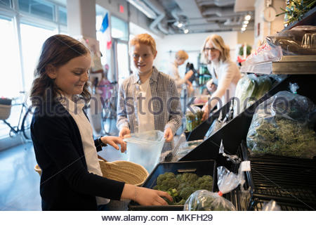 Girl grocery shopping with family, picking out broccoli in market