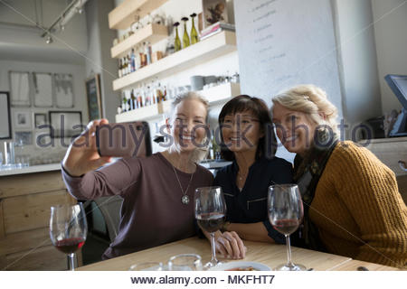 Happy, confident active senior women friends taking selfie with smart phone in cafe