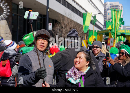 An asian couple pose for a selfie at the Montreal St Patrick's Day parade Stock Photo