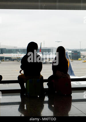 A young boy (5 yr old) sat on his suitcase looking at the planes at Heathrow airport