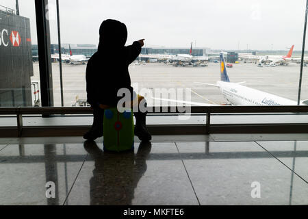 A young boy (5 yr old) sat on his suitcase looking at the planes at Heathrow airport