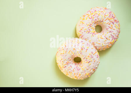 Donut with colorful decor. Isolated on soft green background.Sweet and colourful donuts and cupcakes glazed with sprinkles and frosting. Stock Photo