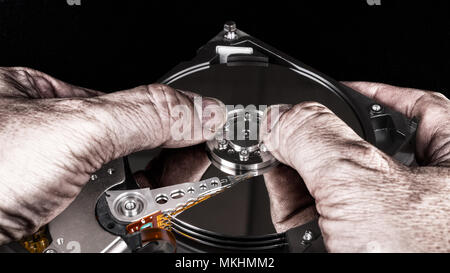 Dirty hands on open hard disk drive. Artistic close-up with mirroring on platter. Black background. Computer saboteur with dismantled storage device. Stock Photo