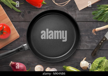 Empty pan on a kitchen table surrounded by vegetarian cuisine ingredients. Stock Photo