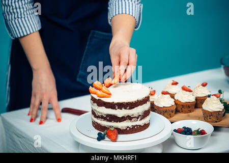 Close up of woman hands decorating chocolate cake with creamy layers with strawberries Stock Photo