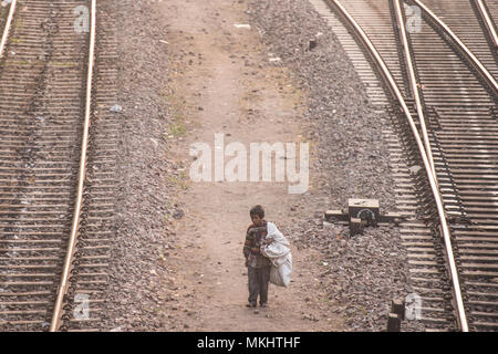 NEW DELHI - INDIA - 14 DECEMBER 2017. A poor child is walking through the railroads looking for something to eat and plastic bottles to recycle. Stock Photo