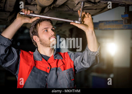 Auto mechanic working at auto repair shop under car with tool Stock Photo