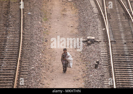 NEW DELHI - INDIA - 14 DECEMBER 2017. A poor child is walking through the railroads looking for something to eat and plastic bottles to recycle. Stock Photo