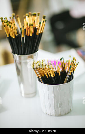 Close up of paint brushes of different sizes in two jars on white table in workshop Stock Photo