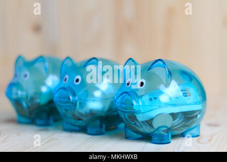 Clear piggy bank with 3 pigs, which has money in it. Placed on a wooden background. Saving money to concept. Select focus shallow depth of field and b Stock Photo