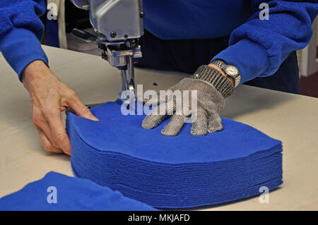 A seamstress uses a vertical knife to cut out a pile of fabric for jackets in a commercial sewing room. Stock Photo