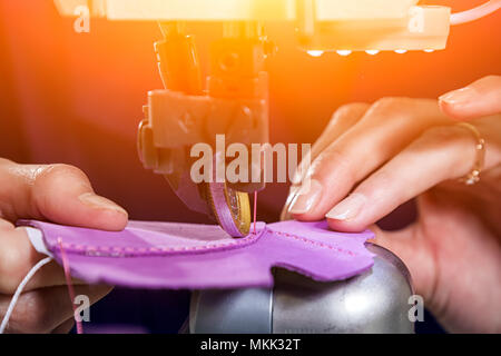 Close-up of a young woman working as a seamstress in a purple unifrome sews genuine leather children's shoes on a sewing machine Stock Photo