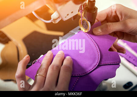 Close-up of a young woman working as a seamstress in a purple unifrome sews genuine leather children's shoes on a sewing machine Stock Photo