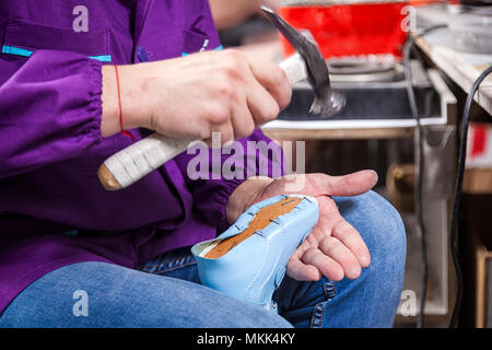 Close-up of a young man worker in jeans makes a soles of children's shoes made of genuine leather, clogs nails in a sewing workshop Stock Photo