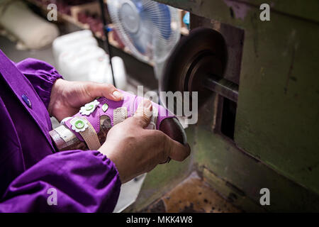 Close-up of a young male worker makes the sole of children's shoes made of genuine leather with a special machine in the sewing workshop Stock Photo