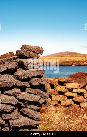 Peat stacks drying in the sun beside a North Uist loch Stock Photo