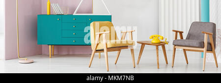 Yellow phone on wooden table next to a grey armchair in vintage living room interior with green cabinet Stock Photo