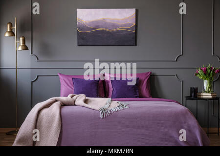 Pink blanket on violet bed in elegant bedroom interior with painting on grey wall with molding Stock Photo