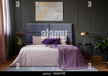 Violet blanket on the bed in pastel bedroom interior with grey poster on grey wall with molding Stock Photo