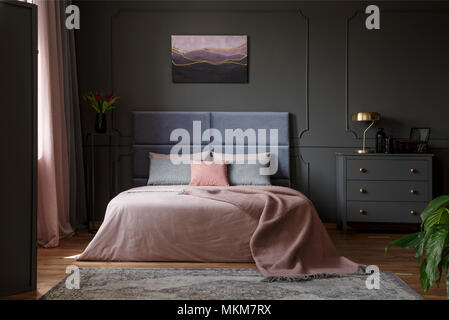 Pastel blanket on bed in pink and blue bedroom interior with gold lamp on grey cabinet Stock Photo