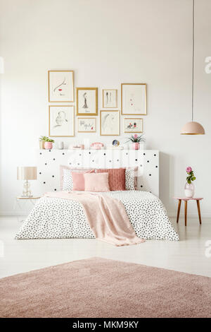 Pink rug and posters in woman's bedroom interior with flower on table next to patterned bed Stock Photo