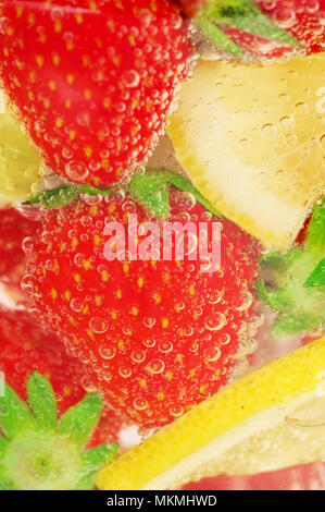 Strawberries and lemons swim in the sparkling water. Homemade lemonade made from strawberry and lemons. Fruit slices in water with air bubbles. Stock Photo