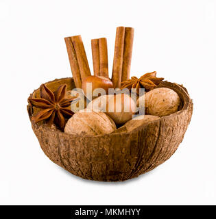 Walnuts, hazelnuts, cinnamon and star anise in a coconut shell. Nuts and spices in a nut shell isolated on white background. Stock Photo