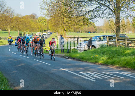 Male cyclists competing in Tour de Yorkshire 2018, racing on flat, scenic, countryside lane, followed by cars - Ilkley, North Yorkshire, England, UK. Stock Photo