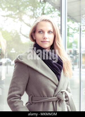 Young beautiful woman standing at a shopping window wearing coat and black shawl Stock Photo