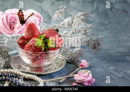 Ripe red strawberry in a glass bowl with pink handmade marshmallows on a beautiful light background with black and white pearls. Copy the space. Stock Photo