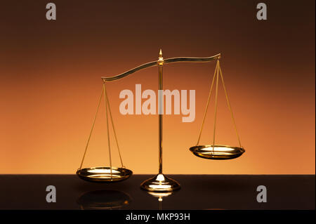 Golden brass balance or imbalance scale on orange color background. Weight balance. Symbol of law justice, libra, decision, crime, financial. Stock Photo