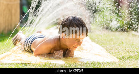 Boy cooling down with garden hose, family in the background Stock Photo
