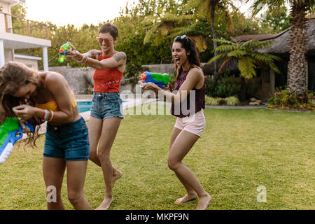 Group of female friends outdoors having fun playing with water guns. Women at pool side playing with water pistols.
