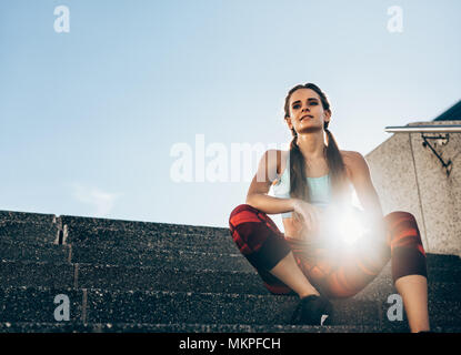 Health young woman sitting on stairs outdoors in morning. Female athlete taking rest after workout with sun flare. Stock Photo