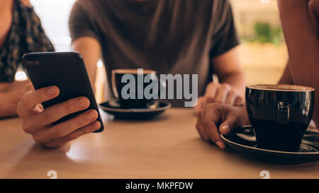 Close up of a smartphone being used by a man sitting at a cafe table with his friends. Young people having coffee and using mobile phone at coffee sho
