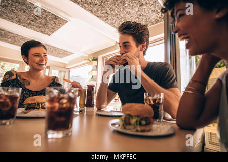 Group of friends meeting at a fast food restaurant. Man and women talking and having stack burger at a restaurant. Stock Photo