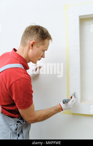 Decorative plaster coating. Man does ragged texture on the wall using a spatula. Stock Photo