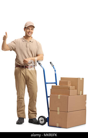 Full length portrait of a delivery man with a hand truck loaded with boxes making a thumb up sign isolated on white background Stock Photo