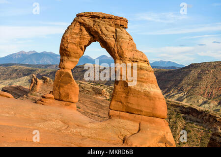 Sunset at Delicate Arch - A close-up view of colorful Delicate Arch in bright evening sun, with rolling rocky mountains in the background, Arches Nat Stock Photo