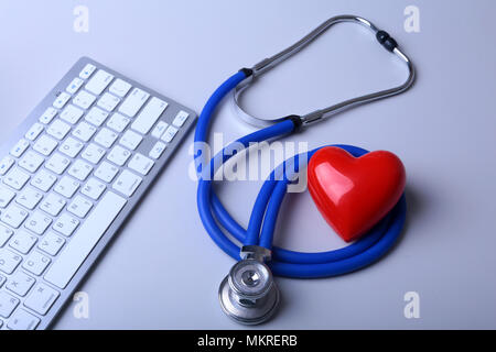 A medical stethoscope with red heart near a laptop on a wooden table. Stock Photo