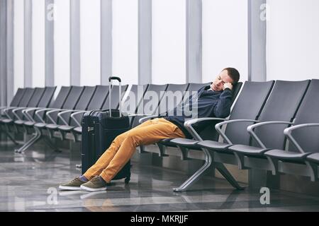 Man traveling by airplane. Tired passenger sleeping in airport terminal. Stock Photo
