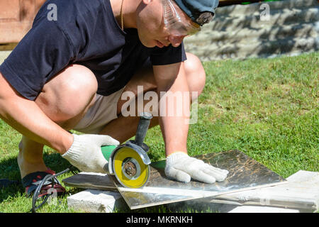 The working tiler cuts the tile with a corner grinder on the floor, movement in the frame, dusty dirty work Stock Photo