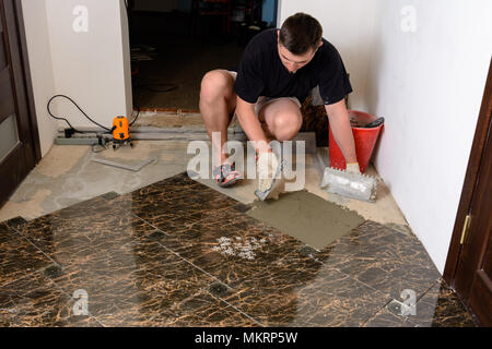 Master man pushes a spatula with a glue solution to the cement surface for laying marble tiles Stock Photo