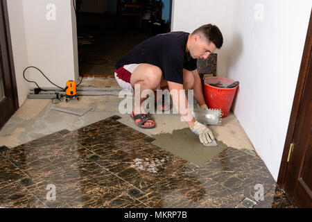 Master man pushes a spatula with a glue solution to the cement surface for laying marble tiles Stock Photo