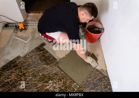 Master man pushes a spatula with a glue solution to the cement surface for laying marble tiles Stock Photo